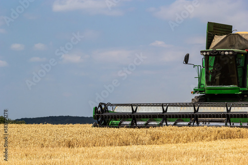 Photo of combine harvester that is harvesting wheat with dust straw in the air