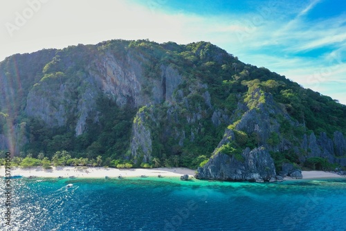Panorama drone shot of the paradisiacal beach of Coron, Palawan in the Philippines with fine white beach, palm trees and majestic rocks.