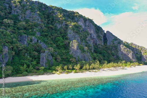 Panorama drone shot of the paradisiacal beach of Coron, Palawan in the Philippines with fine white beach, palm trees and majestic rocks.