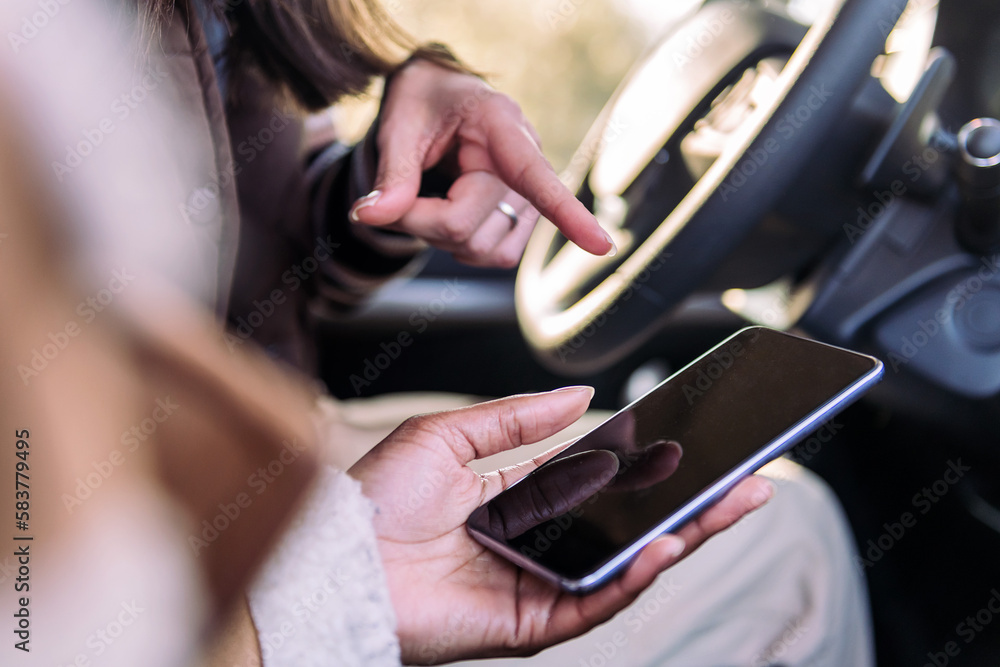 close up of the hands of two young women using road navigation at phone on a road trip, concept of adventure and travel technology