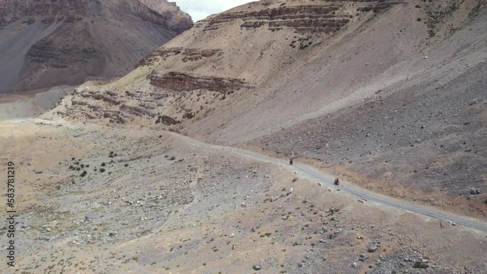 aerial tracking shot of two motorcyclists driving fast down a dry rugged mountain on a sunny day in Spiti Valley India aerial tracking shot of two motorcyclists driving fast down a dry rugged mountain on a sunny day in Spiti Valley India