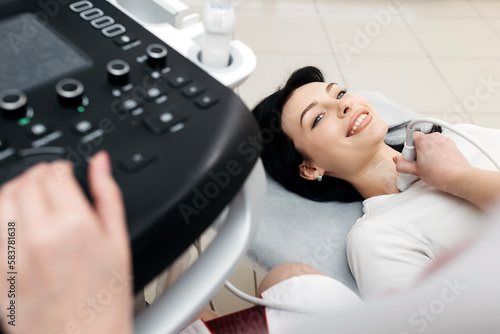 The doctor diagnoses the thyroid gland of the patient with the help of an ultrasound scanner, top view. woman lies on the sofa. A woman holds an ultrasonic probe along the patient's neck in a clinic.