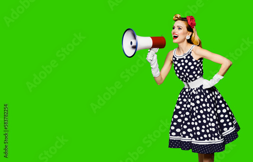 Portrait image of beautiful woman holding mega phone, shout advertising. Pretty girl in black pin up dress, white glows with megaphone loudspeaker, green chroma key background. Big sales ad.