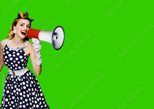 Portrait image of beautiful woman holding mega phone, shout, saying, advertising. Pretty girl in black pin up style dress with mega phone loudspeaker, green chroma key background. Big sales ad.