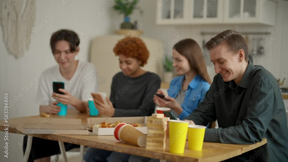 Four friends sit in home kitchen look at mobile screen. Men and women ignoring each other, boring meeting. Together using phone gadget. Concept modern problem internet addicted with social network.