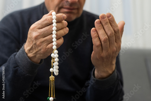 Praying hands of an old man holding rosary beads.