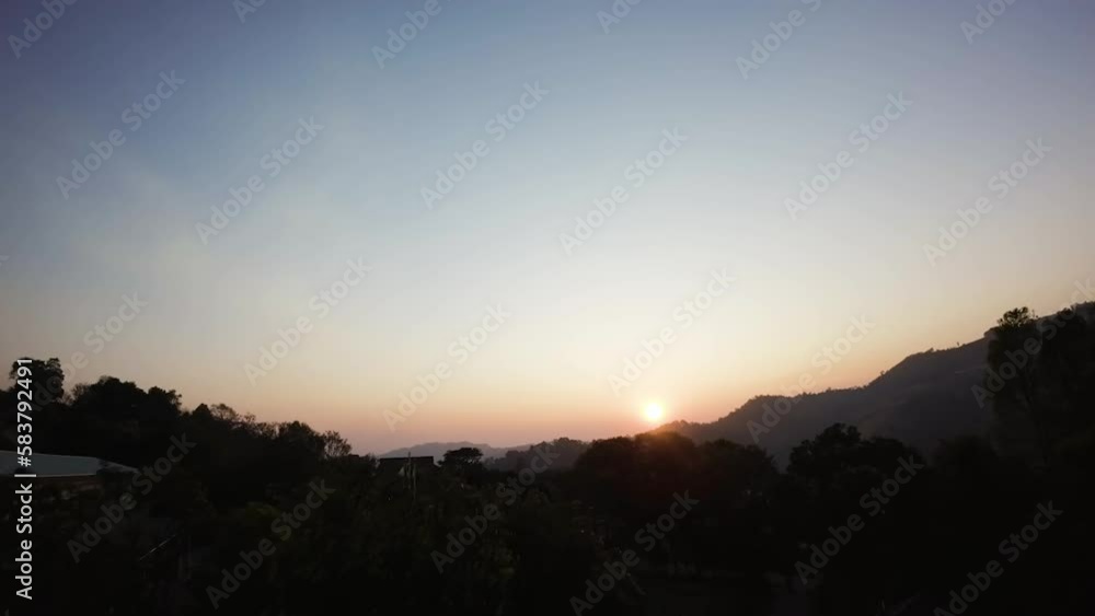 Slow motion silhouette FPV shot above trees revealing the sun setting behind a mountain Slow motion silhouette FPV shot above trees revealing the sun setting behind a mountain