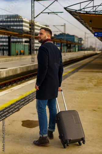 Young man waiting for a train with his suitcase in hand, he's going on a business trip