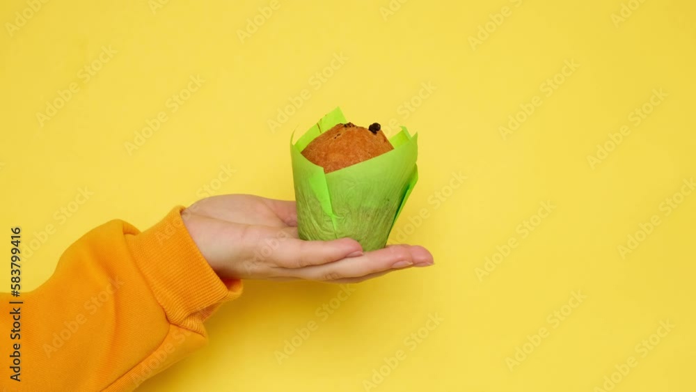 Muffin in green paper wrapper and hand on yellow background Muffin in green paper wrapper and hand on yellow background