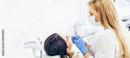 Female dentist with female patient in dental chair providing oral cavity treatment.