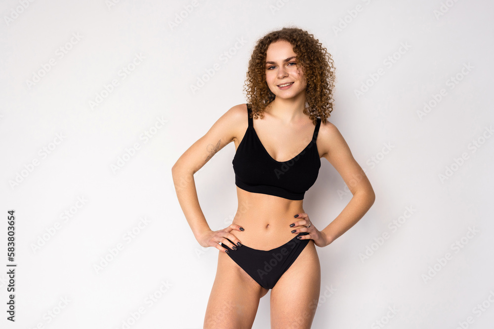 Fototapeta premium Cheerful attractive young fitness woman in black top and black lingerie over white background