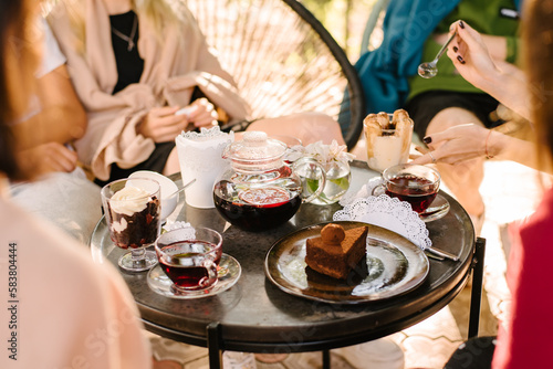 Terrace of the summer cafe. on the table are glass cups with tea, a glass teapot with fruit tea and desserts. The girl in her hands holds a spoon and is going to eat dessert