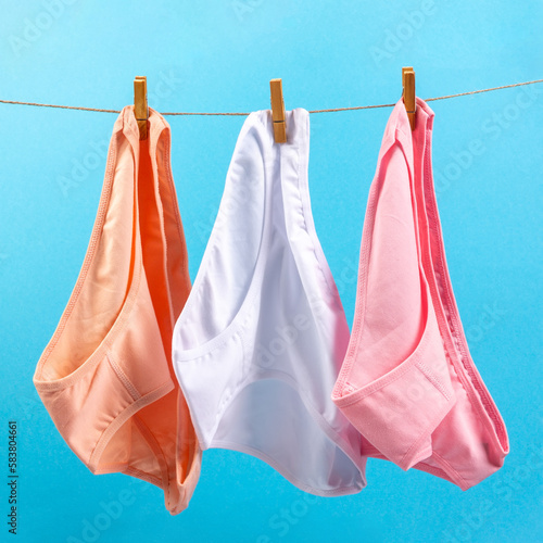 washed women's panties made of cotton with clothespins hanging on a rope on a blue background