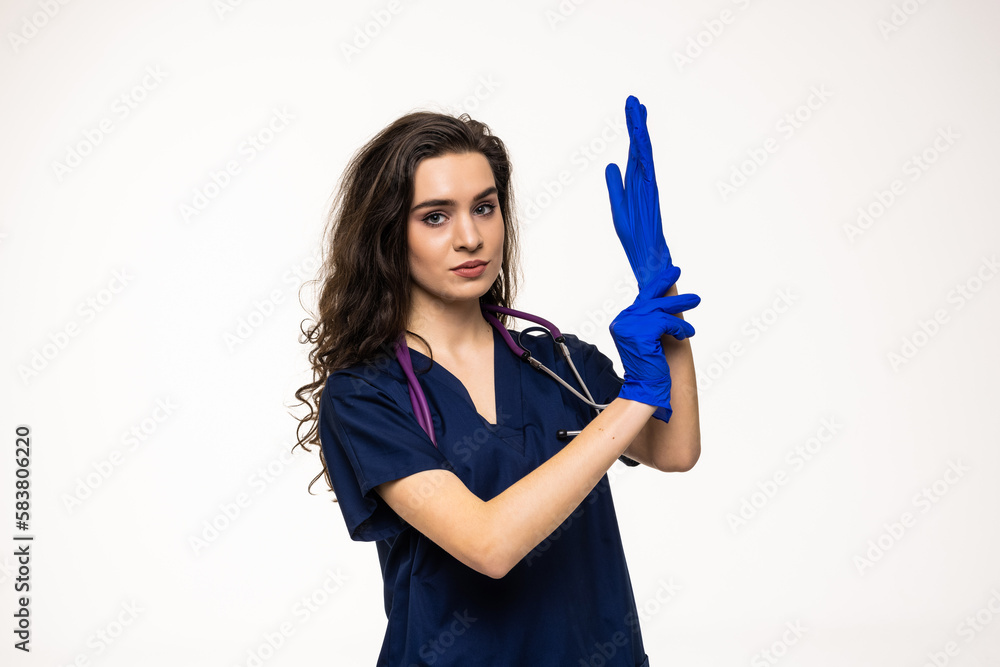 Portrait of young female doctor posing on white background, putting gloves on hands Portrait of young female doctor posing on white background, putting gloves on hands