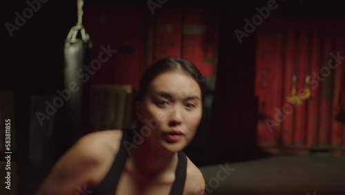 Portrait of determined concentrated sporty fit attractive Asian female boxer in boxing gloves shadowboxing, training, and improving punching techniques, throwing uppercut and jab in gym.