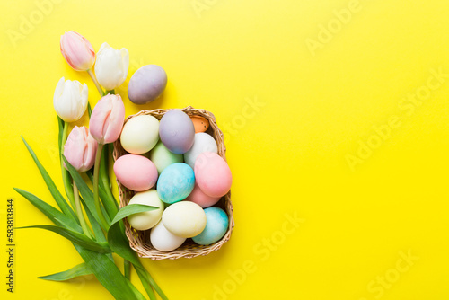 Happy Easter composition. Easter eggs in basket on colored table with yellow Tulips. Natural dyed colorful eggs background top view with copy space