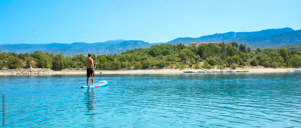 Man standing on paddle on blue lake in France- Verdon