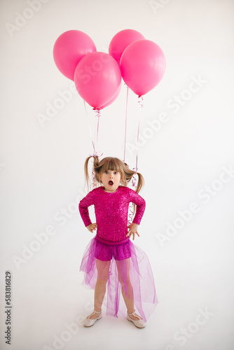 Cute happy child girl 4-5 year old wear princess dress posing with balloons having birthday party over white in room. Childhood.