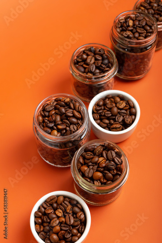 Aromatic roasted arabica and robusta coffee beans in glass small jars on bright orange background. Perfect coffee beans to make tasty coffee beverages such as espresso, americano, cappuccino, latte.