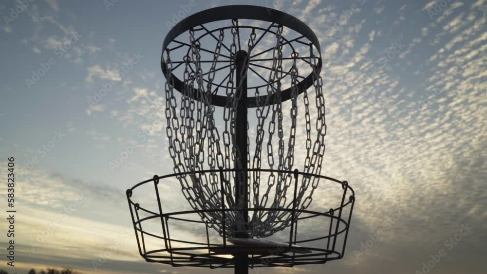 2 Discs Simultaneously Go into Disc Golf Basket that is Silhouetted by the Late Evening Sky with Beautiful Clouds 2 Discs Simultaneously Go into Disc Golf Basket that is Silhouetted by the Late Evening Sky with Beautiful Clouds