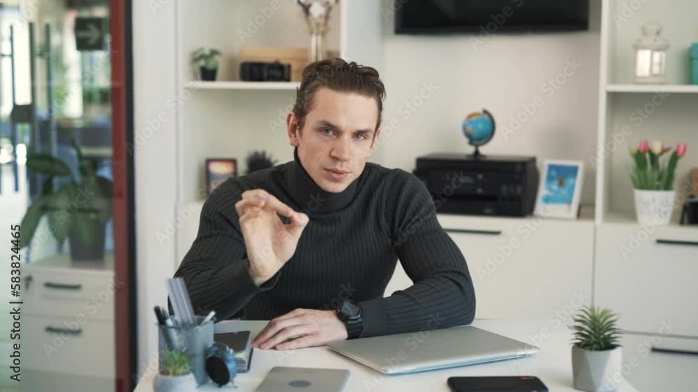 The man is sitting at a table and talking to the camera,gesturing with his hands, then he starts laughing and shows a thumbs-up gesture.The man is sitting in an office at a table The man is sitting at a table and talking to the camera,gesturing with his hands, then he starts laughing and shows a thumbs-up gesture.The man is sitting in an office at a table