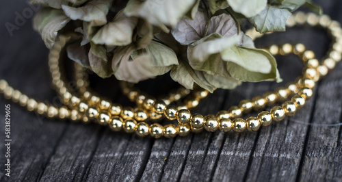 The photo shows hematite beads. This is a natural stone painted in different colors, round and hexagonal. Placed on a wooden board on a background of dried hydrangeas.