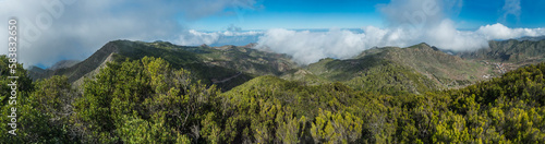 Panoramic view from Baracan mountain. Green forest, hills and valley with terraced fields and village Las Portelas at Park rural de Teno, Tenerife, Canary Islands, Spain. sunny day, blue sky