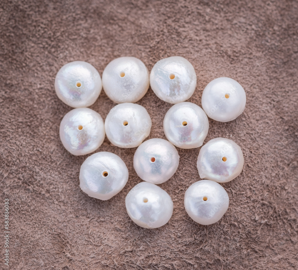 Natural freshwater pearls of various shapes and colors are photographed on a wooden board and a piece of leather. Natural freshwater pearls of various shapes and colors are photographed on a wooden board and a piece of leather.