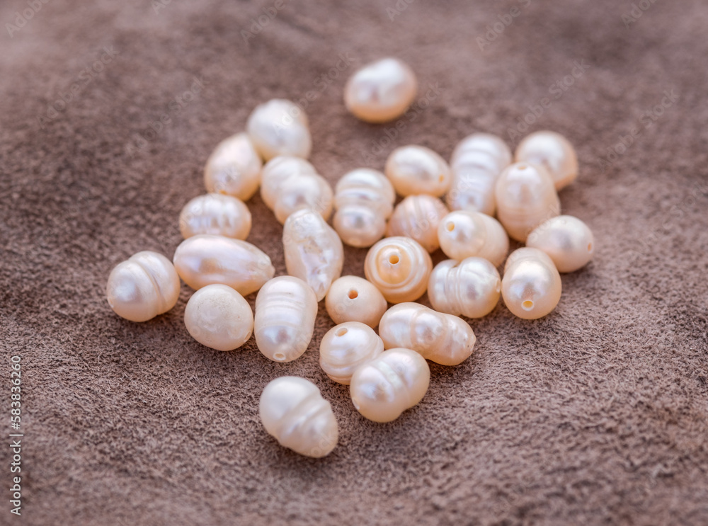 Natural freshwater pearls of various shapes and colors are photographed on a wooden board and a piece of leather.