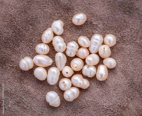 Natural freshwater pearls of various shapes and colors are photographed on a wooden board and a piece of leather.
