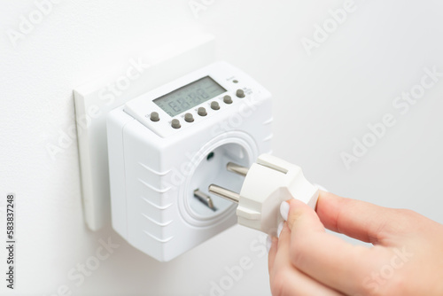 Close up of woman hand inserting plug to the socket timer, computer. Controlling usage of electricity by using smart outlet adapter