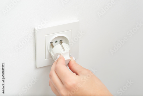 Hand of a woman plugging in an electric cord into a white european socket. Turning on an electric instrument, inserting electric plug