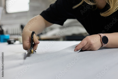 Dressmaker in a smart watch cuts a piece of fabric with scissors in a sewing workshop. Production of piece of modern clothing or upholstery for upholstered furniture made of fabric in studio workshop