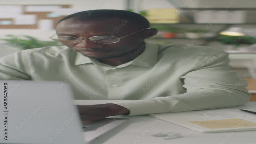 Vertical shot of African American businessman typing on laptop while working at desk in office Vertical shot of African American businessman typing on laptop while working at desk in office
