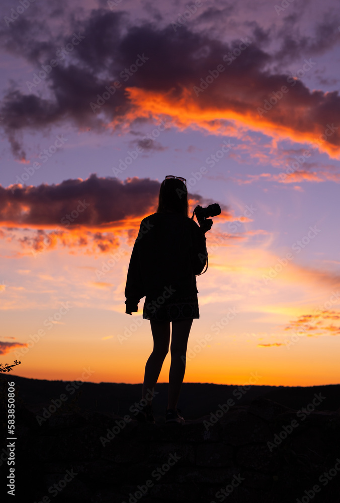 Silhouette of woman holding camera at sunset