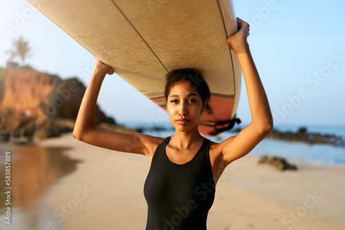 Canvas Print African american woman standing with surfboard on head on ocean beach