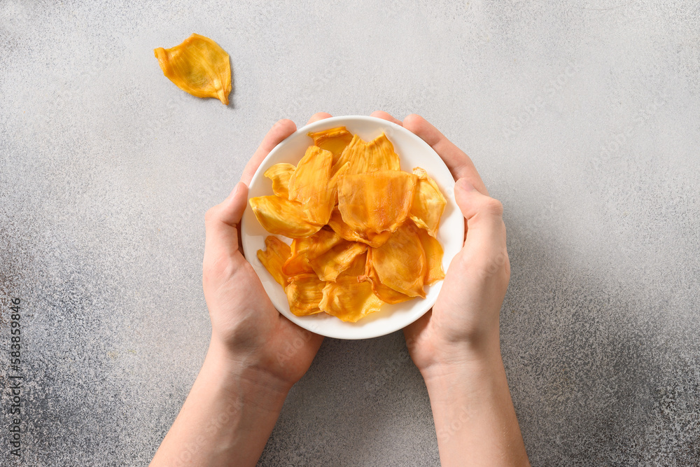 Holding jackfruit chips in white plate on gray background. Fruits chips for vegan with antioxidant, vitamin from tropical island Ceylon. Top view. Local food and sugar free tasty snacks. Holding jackfruit chips in white plate on gray background. Fruits chips for vegan with antioxidant, vitamin from tropical island Ceylon. Top view. Local food and sugar free tasty snacks.