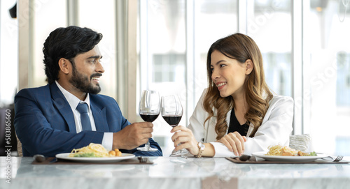 Beard man and beautiful woman drink wine to celebrate love anniversary. Young romantic couple happy dinner in luxury restaurant. Asian woman dating Indian man and have fun drinking alcohol together. © Nassorn
