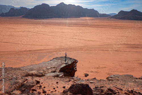 A person standing on a rock above the wide plain of Wadi Rum desert, UNESCO World Heritage Site, Jordan