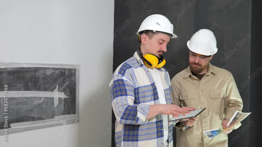 The chief engineer at the construction site explains to the installer the work plan on an electronic tablet. Two engineers on a construction site indoors. High quality 4k footage The chief engineer at the construction site explains to the installer the work plan on an electronic tablet. Two engineers on a construction site indoors. High quality 4k footage