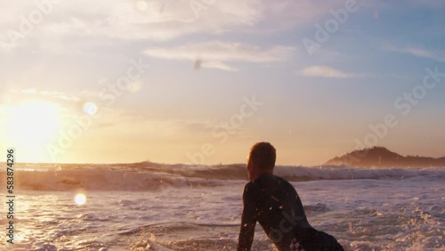 Surfer goes with surfboard in the ocean at sunrise