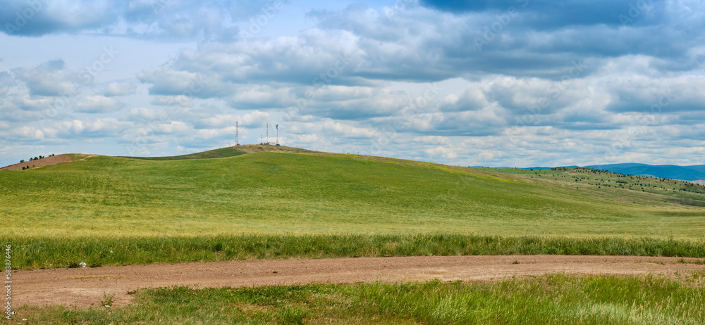 Bald Mountain in the Buryat Republic of Russia. Green hills against a blue sky with clouds.