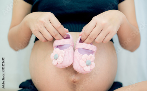 Pink baby shoes and pregnant woman,Pregnant woman expecting daughter. Expectant mother applying pink baby shoes to belly. Maternity concept © banjongseal324