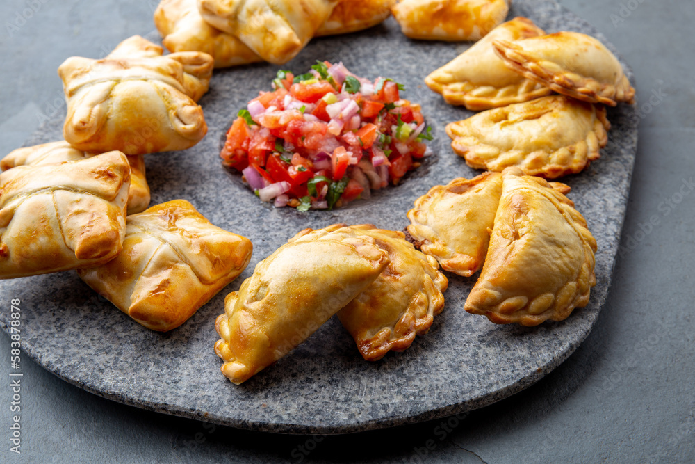 Different little cocktail EMPANADAS on stone plate with tomato sauce and guacamole . Gray background. Latin American and Spanish tipical food Different little cocktail EMPANADAS on stone plate with tomato sauce and guacamole . Gray background. Latin American and Spanish tipical food