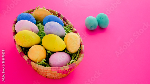 Colorful bright  Easter eggs inside basket on pink background