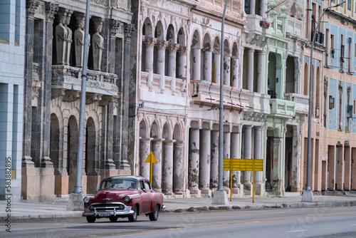 Faded grandeur, stucco, weather-beaten houses on seafront of Malecon, with red classic car, Havana photo