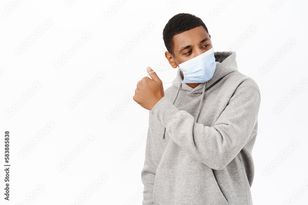 Image of african american man takes off medical face mask, stands in hoodie over white background Image of african american man takes off medical face mask, stands in hoodie over white background