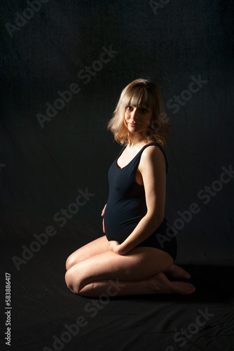 Pregnant woman with big belly in bodysuit,lingerie on black background. Sexy attractive girl photoshoot in studio. Happy pregnancy,maternity,preparation.Baby expectation.Beautiful tender young mother