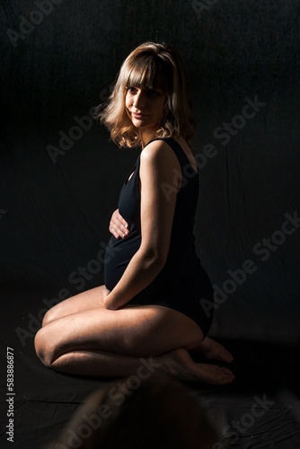 Pregnant woman with big belly in bodysuit,lingerie on black background. Sexy attractive girl photoshoot in studio. Happy pregnancy,maternity,preparation.Baby expectation.Beautiful tender young mother