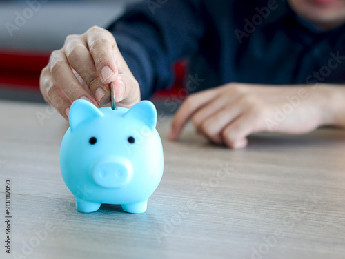 Hand man collecting coins in blue piggy bank on desk, finance savings or investment for the future concept.